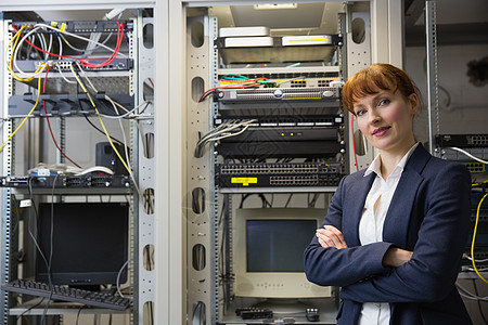 漂亮的计算机技师在服务器旁边的相机上微笑女性储物柜数据电脑路由器技术员力量程序员电缆双臂图片