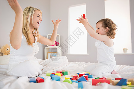 母亲和女儿在床上玩砖块的游戏建筑快乐卧室头发房子家庭积木童年孩子女性图片