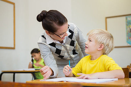 美貌教师帮助教室中的学生铅笔小学生微笑早教班级课堂瞳孔混血男性童年图片