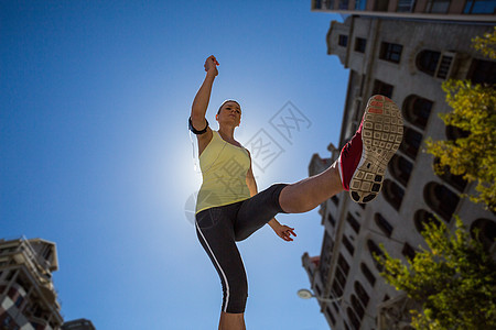 一个美丽的女人在街上跳跃晴天运动服都市训练蓝天女士运动专注路面护理图片