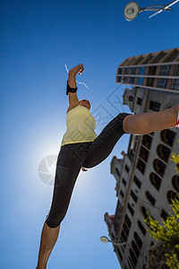 一个美丽的女人在街上跳跃运动护理专注训练都市女士运动服阳光蓝天运动员图片