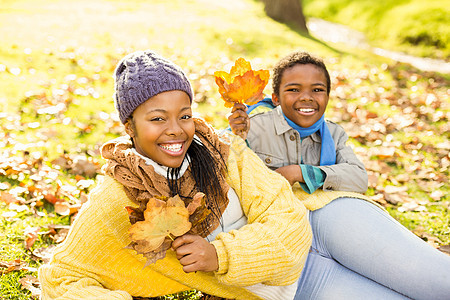 年轻母亲和儿子坐在树叶上微笑快乐衣物女士草地农村公园绿地童年环境图片