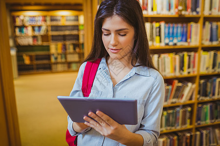 布莱奈特学生在书架旁边使用平板电脑文学大学红色图书馆女性药片专注教育知识学习图片