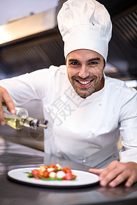英俊的厨师在饭上浇橄榄油餐饮男人商业工作职业大楼厨房盘子微笑制服图片