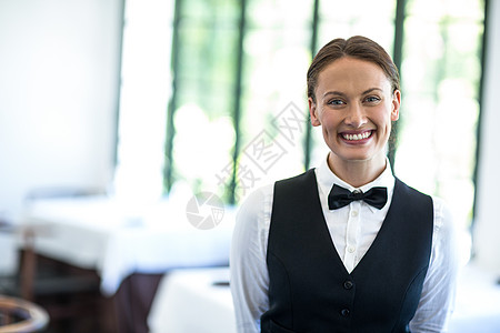 快乐的女服务员在相机上微笑套装女士服务衬衫马甲领结餐厅酒店头发女性图片