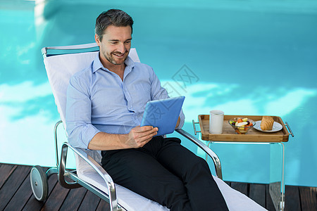 智能人使用靠近游泳池的数码石板电脑微笑男性空闲假期食物时间泳池茶几面包图片