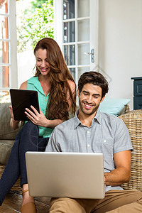 在客厅使用数字平板电脑和笔记本电脑的夫妇微笑女士女性闲暇快乐沙发滚动技术夫妻互联网图片
