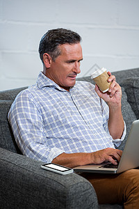 男人在喝咖啡时使用笔记本电脑电话职场沙发电子技术企业家饮料手机休闲男性白种人高清图片素材