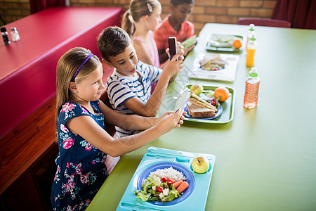 儿童午餐时使用技术的儿童男性幼儿园同学们水果教育小学女性食堂男生素食者图片