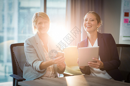 利用数字平板电脑和移动电话进行互动的女商务人士微笑会议触摸屏领导职场同事伙伴沟通战略人士图片