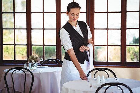 微笑的女服务员摆桌子工作餐巾椅子盘子工人制服女士酒店马甲刀具图片