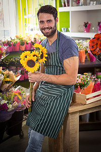 向日葵微笑男花匠在他的花店里拿着一束鲜花背景