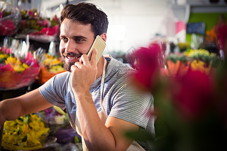 解讲员男花店员在移动电话上说话沟通花园中心讨论桌子失速职业呼唤男性花朵背景