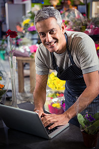 使用膝上型电脑的男花店花艺笔记本花园中心围裙零售头发花朵桌子盆栽图片
