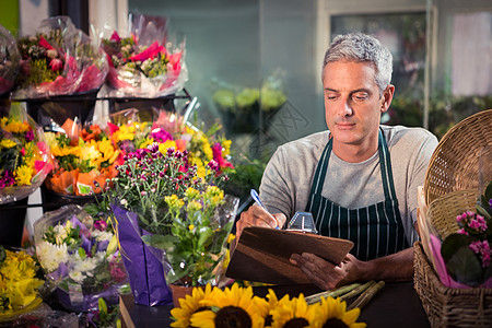 在剪贴板上写字的男花匠花束向日葵写作花艺零售中心植物清单桌子头发图片