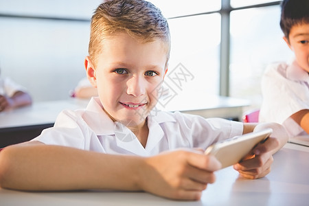 在课堂上使用移动电话的在校儿童男生金发女郎微笑快乐桌子手机校服教育电话男性图片