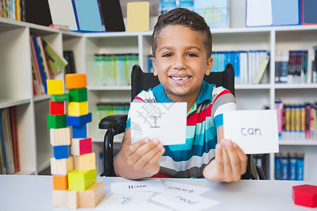 残疾男孩显示在图书馆里读到的标牌快乐成功建筑男生混血小学学习学生微笑桌子图片