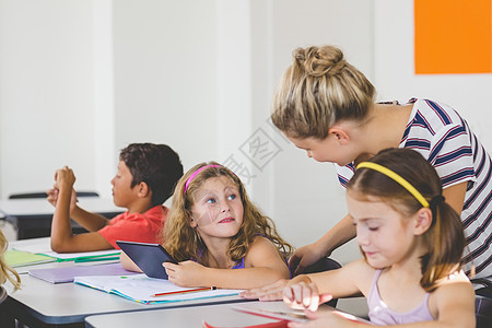 教师在数字平板电脑上教孩子孩子们学校女孩服装滚动快乐阅读休闲学习学生图片