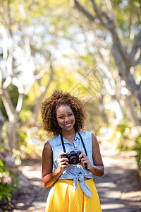 微笑的女人用数码相机站立公园农村童年摄影师活动绿地混血快乐技术闲暇图片