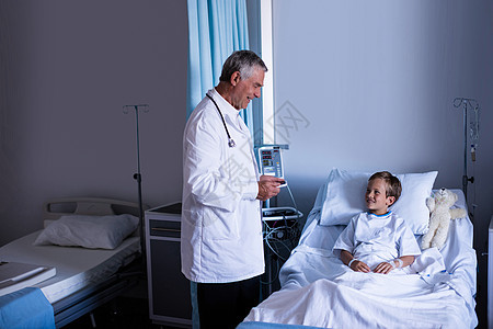 男性医生在病房看病期间与病人进行互动医院孩子咨询医师病床平板医务室网络专家电脑图片