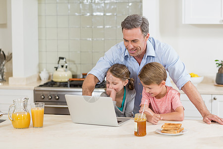 父亲和孩子在吃早餐时使用笔记本电脑闲暇玻璃台面儿子生活男人饮料亲密感快乐房子图片