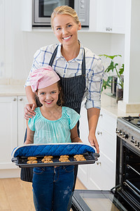 幸福的母亲和女儿在厨房里拿着烤饼干盘子家庭生活亲密感微笑服装女士住所公寓准备孩子烤箱图片