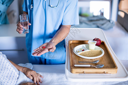 医生为床上女高级病人提供药物治疗托盘玻璃男性服务药品医院茶点勺子男人卫生图片