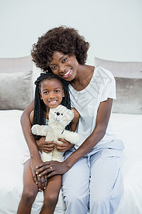 母亲和女儿在家中带着双臂坐在床上微笑着笑图片