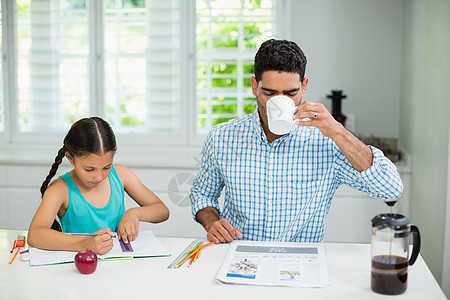 女儿在做家庭作业 父亲在看报纸时喝杯黑茶(black tea)图片
