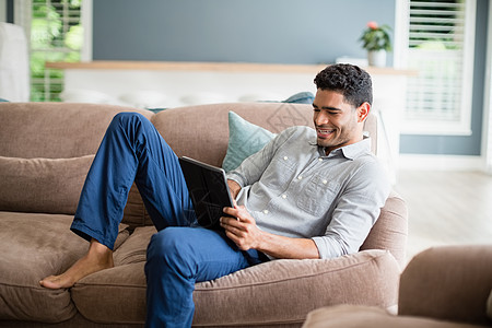 坐在沙发上和在客厅使用数字平板电脑的人数位板现实男人闲暇滚动阅读混血房子住所家庭图片