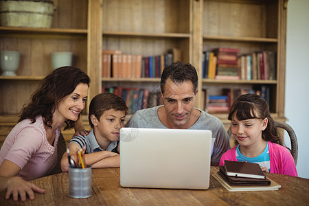 在学习室桌上使用笔记本电脑的父母和孩子父亲男性女士技术住所家庭生活男生笔筒女孩家庭图片