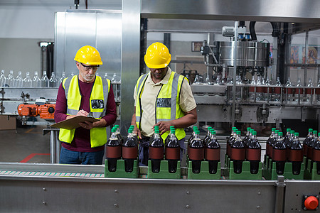两名工厂工人在工厂内监测冷饮瓶子的工作商业男人技术男性现实生产机器包装工作服生活图片