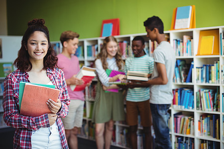 快乐的男学生在图书馆藏书的肖像女学生教育青年服装女性童年闲暇书架女孩学校图片