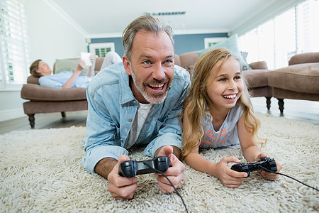 快乐的父亲和女儿躺在起居室地板上玩电玩游戏时微笑现实科技游戏房子休闲家庭生活乐趣俏皮遥控图片