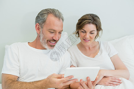 夫妇在卧室床上使用数字平板电脑微笑图片