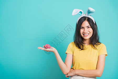 女人笑着白牙 穿着黄色T恤和兔子站立手势女孩女士粉色蓝色耳朵手指庆典工作室快乐图片