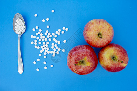 蓝底苹果旁边的一勺子和补充维生素片药片图片