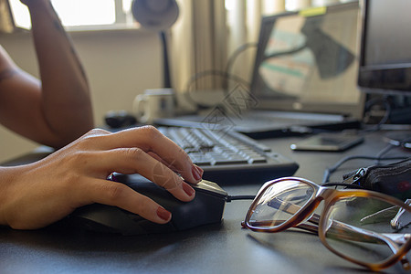 使用计算机和眼镜 键盘 笔记本电脑和监视器对一名妇女进行近身检查 并在背景上显示办公室工作手指管理人员学习纽扣指甲网络技术商业图片
