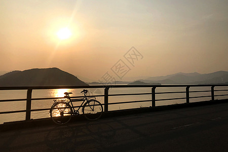 太阳日落时环绕海洋的双轮长休式自行车和围篱图片