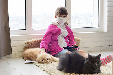 一个被隔离的生病女孩坐在地板上 拿着平板电脑 猫躺在地毯旁边图片