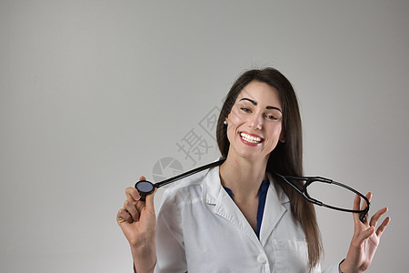 女性医疗专业人员在颈部周围带着听诊器 脖子被灰色隔绝 笑容美丽的年轻女子很吸引人爆头血压保健照顾者女士医师博士护理药品老年图片