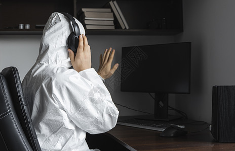 身穿医用口罩和防护服 戴手套的男子坐在家里 在检疫期间与桌上的电脑一起工作 并向他的商业伙伴或朋友问好 大流行病中的远程工作诊断图片