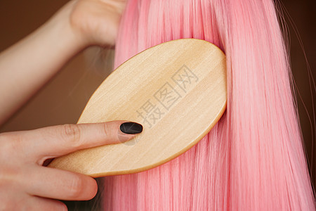 女性手握长发的粉红色假发 用木梳子梳头图片