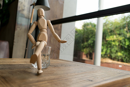 人坐在水的杯上娃娃咖啡木偶木头玩具身体男性姿势玻璃桌子图片