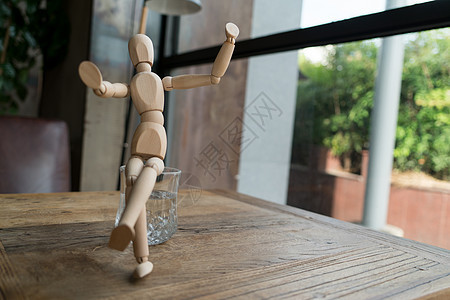 人将坐在水的杯上 手举起玻璃杯子男人咖啡模型娃娃木偶玩具人体木头图片