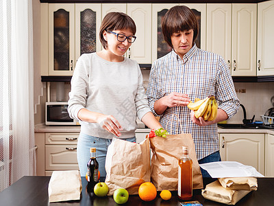 年轻夫妇正在厨房整理购买物品 产品一i送货互联网牛皮纸女性丈夫男人妻子家庭成人水果图片