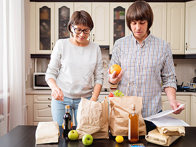 年轻夫妇正在厨房整理购买物品 产品一i互联网女士男人橙子夫妻丈夫成人妻子牛皮纸水果图片