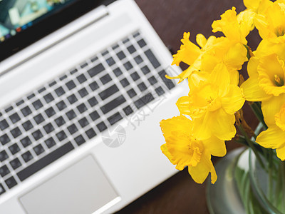 银金属笔记本电脑上的玻璃花瓶中的Narcissus或水仙 带便携式装置的亮黄色花朵 Wooden背景水仙花桌子花店植物群互联网职图片