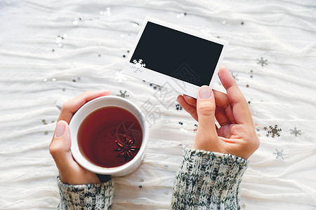 女人握着一杯茶和照片 冬季布料背景有闪亮的银雪花 文字或图片上没有照片框 掌声框架饮料白色风格织物假期装饰杯子边界新年图片