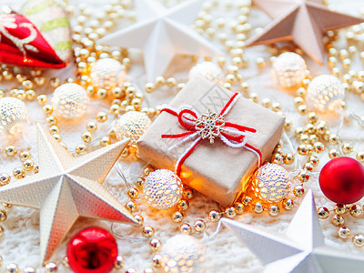 白色针织背景上的圣诞节和新年明星装饰品 用牛皮纸包裹的礼物盒 上面有雪花符号 金属灯泡有精致的图案 金珠 红球图片